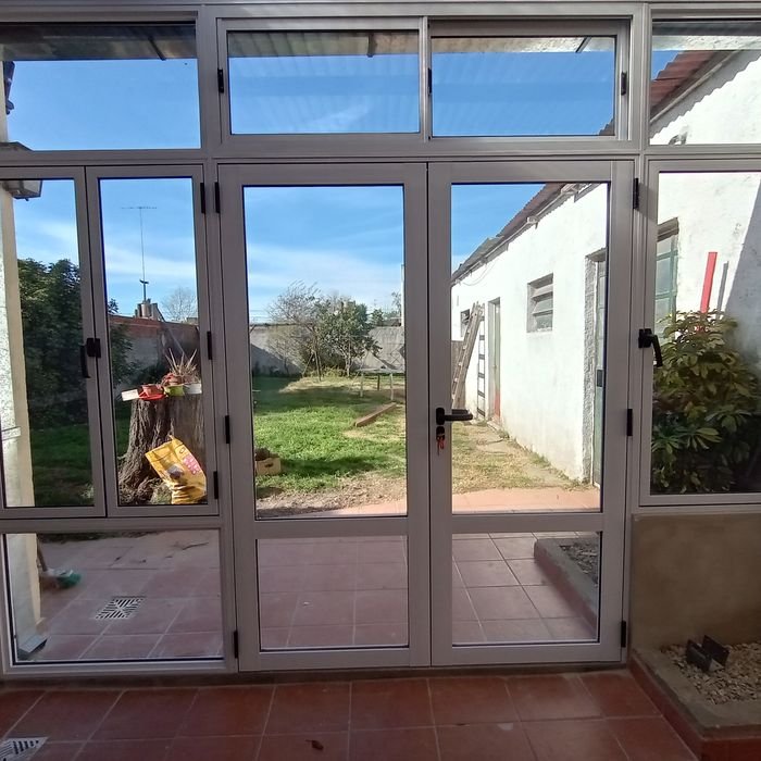Cerramiento blanco con puerta, corrediza y paños fijos bajo techo de policarbonato