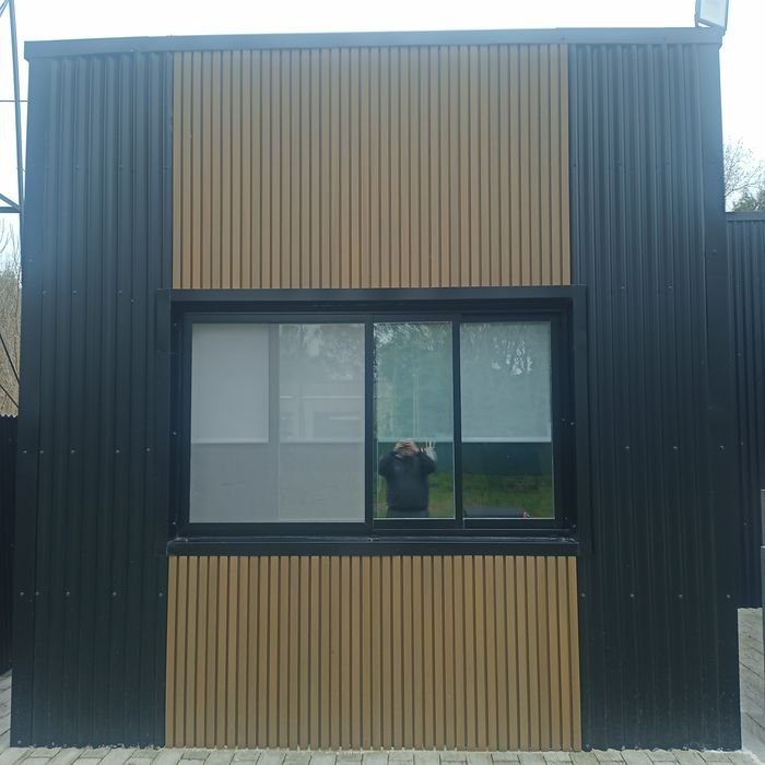 Ventana de aluminio negro sobre fachada de chapa y madera